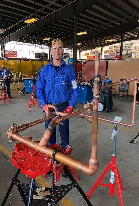 A smiling man stands behind a display of joined copper joints